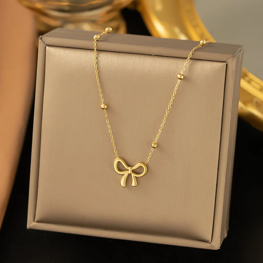 A gold necklace with a bow-shaped pendant and small bead accents, displayed on a beige jewelry box.