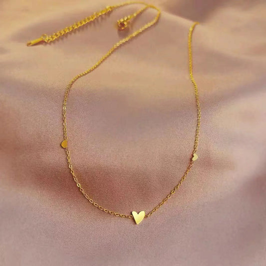 Gold necklace with a heart pendant on a soft pink background