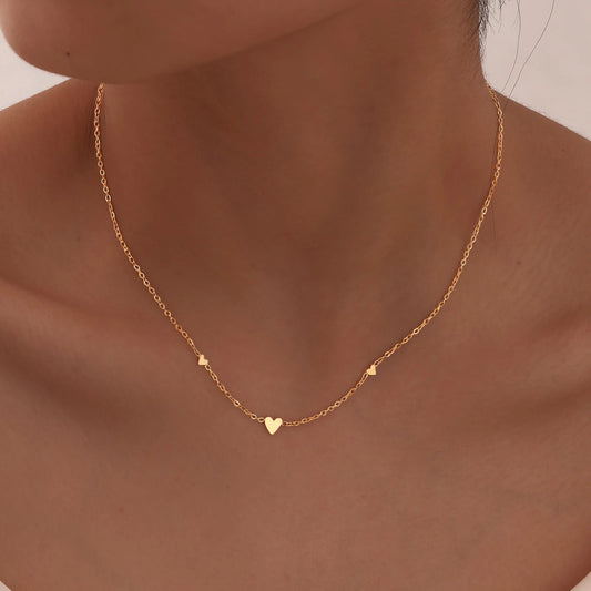 Gold necklace with heart pendants on a person's neck against a neutral background