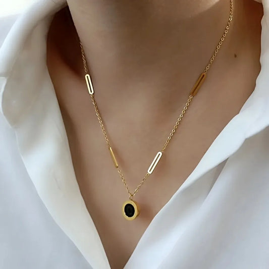 Gold necklace with a black pendant on a white background