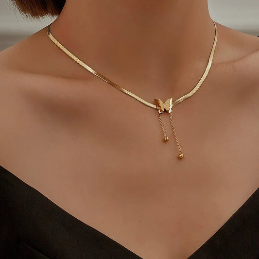 A gold snake chain necklace with a butterfly charm and dangling chains, shown worn on a model's neck.